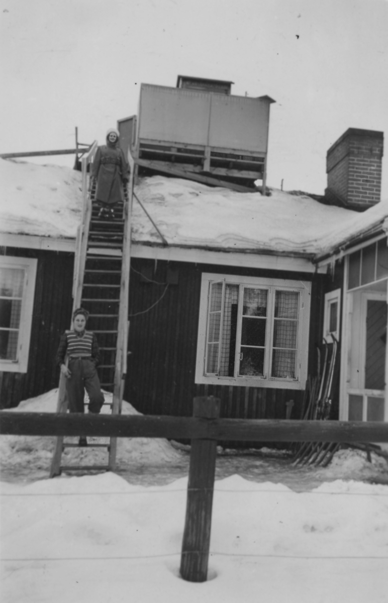 Luftbevakningsstationen tillhörande 91:a ls-kompaniet i Tellejåkk, Kåbdalis, 1942. Luftbevakningstornet var placerat direkt på taket på förläggningen. Frivilliga luftbevakarna Birgit Johansson (i uniform) och Karin Nordberg. Exteriör.