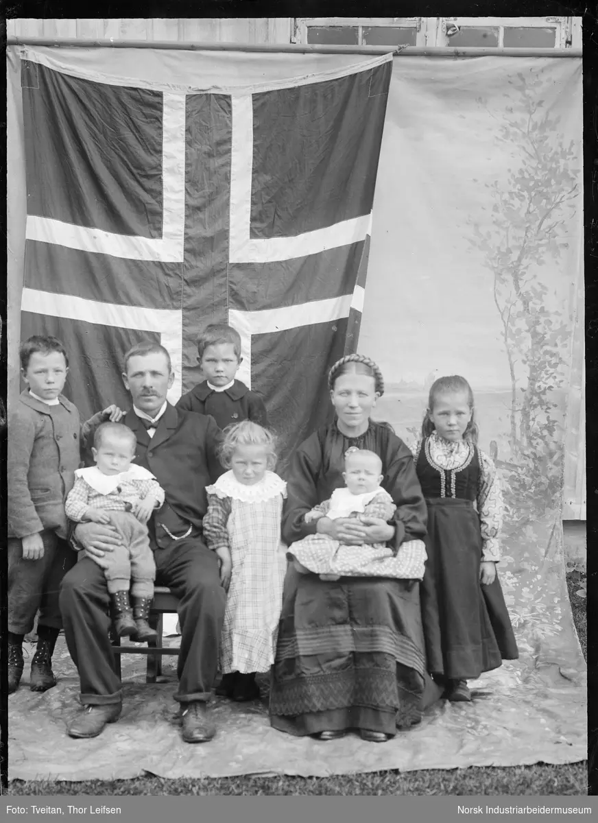 Gruppefoto. Familie med åtte personer foran det norske flagget.