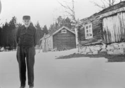 Eldre mann står ute foran to bygninger, huset i Søre Lykkja 