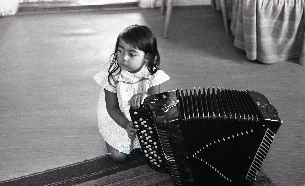 En liten flicka sitter på golvet intill ett dragspel. Bilden är tagen i samband med ett nyhetsreportage för Skånska Dagbladet. Att vara musikant har historiskt varit ett vanligt yrke bland romer i Sverige.