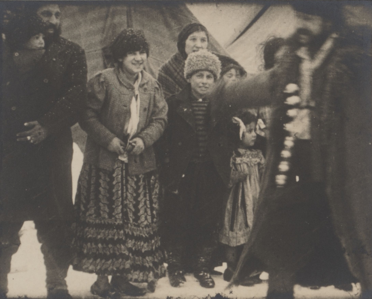 Människor i olika åldrar har samlats utanför sina bostadstält. De tillhör den grupp romer som folkvandrar genom Europa under 1800-talets andra hälft och kommer till Sverige via Ryssland och Finland.