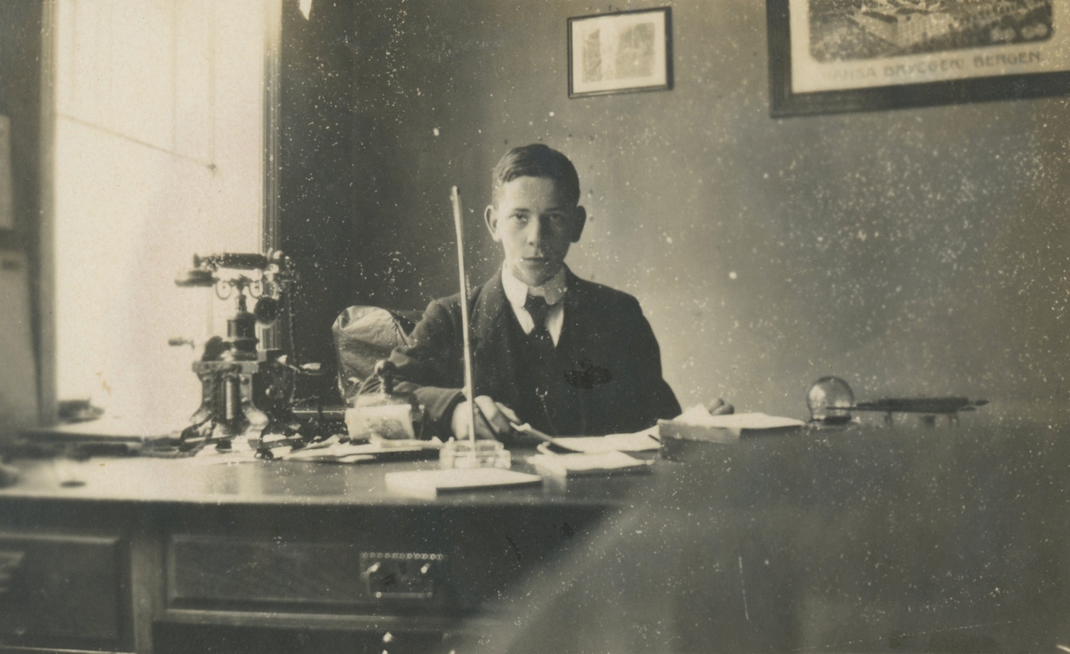 Portrettfotografi av en ung mann som sitter bak en kontorpult.