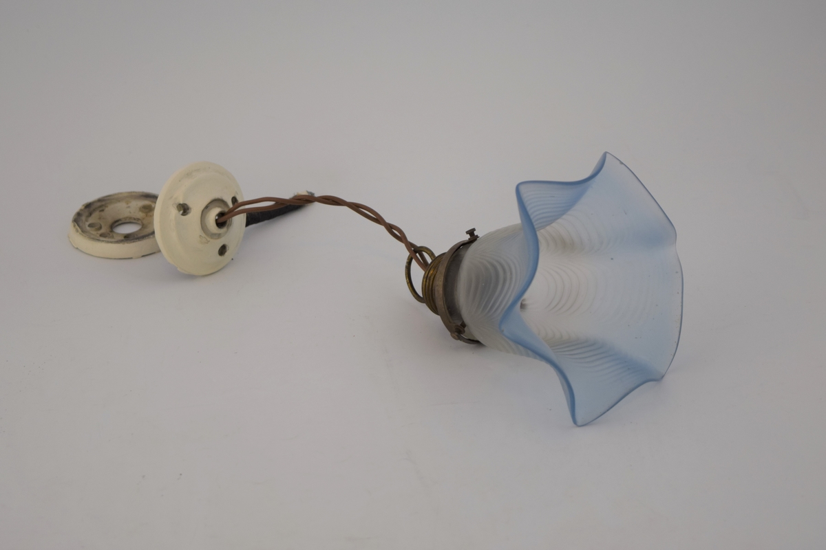 Elektrisk taklampe med klokkeformet lampeskjerm av transparent blått glass. Støpsel til en lyspære. Takfeste av porselen som senere har blitt overmalt - i to deler.