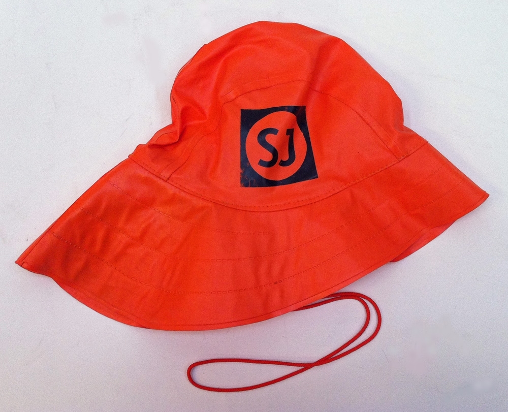 Orange sydväst av PVC. SJ logotyp på ena sidan. Vitt foder med öronlappar. Hakband bestående av ett orange snöre.
Inuti mössan sitter en lapp med storlek 58 samt en lapp med tillverkarens namn, Abeko samt tvättrådet 40 grader och "Made in Finland".
