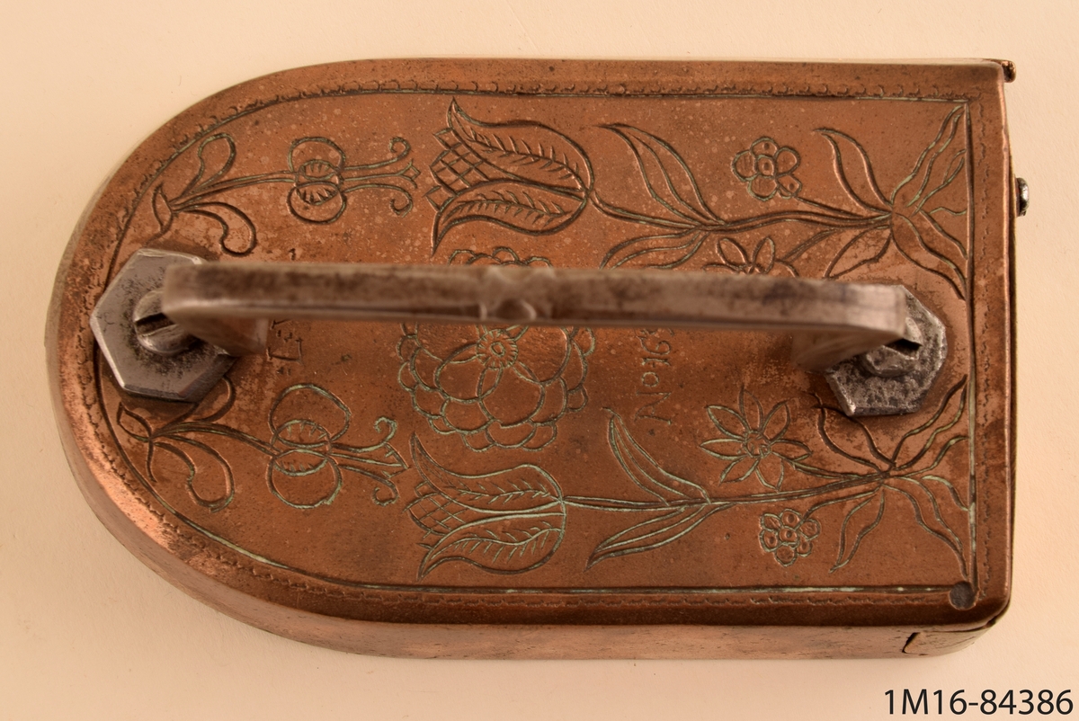 Strykjärn av kopparlegering. På ovansidan ett handtag i järn fäst med två skruvar i underdelen som är blomdekorerad på ovansidan. Märkt: :L:W: No.1697.
