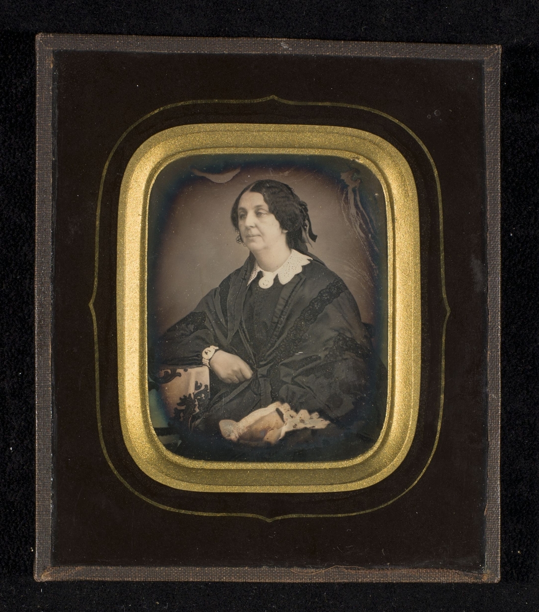 Daguerreotypi av kvinne ikledd sort silke, sittende ved et bord.