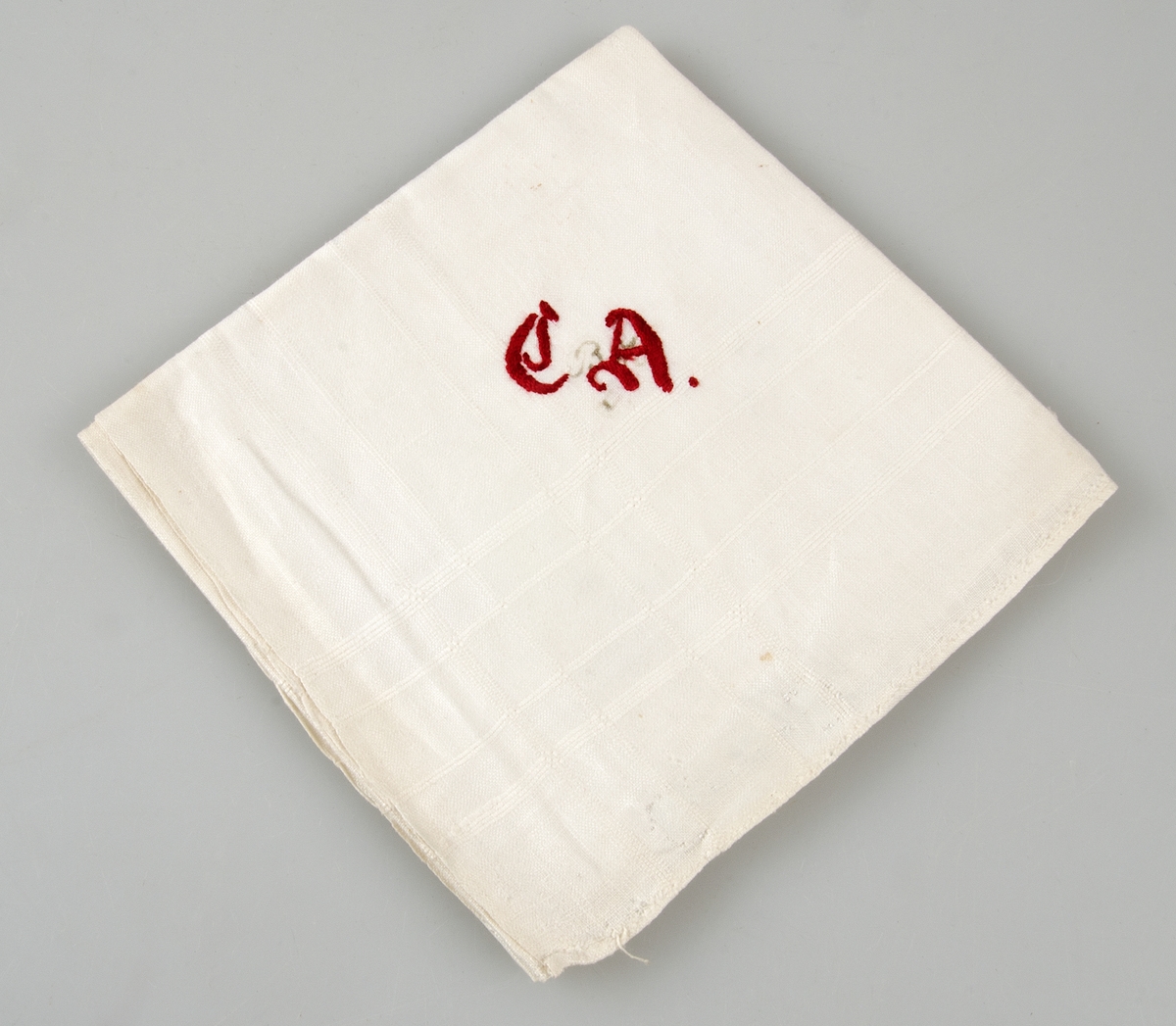 Av vit linnelärft med invävd kantbård. Rött monogram i plattsöm och stjälkstygn. Med märkbläck B H. Handfållad på två sidor.