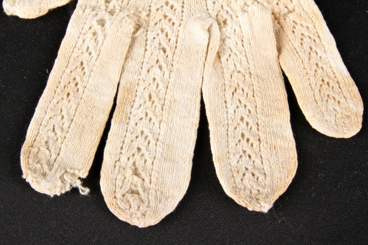 Hvite, mønsterstrikkede bomullsvanter. Strikket av tynt bomullsgarn, hvor hullstrikk danner mønsteret. På håndbaken er det i hullmønsteret laget initialene M A på den høyre vanten, og årstallet 1822 på den venstre. 