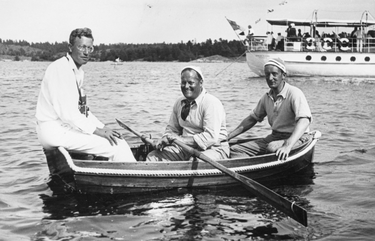 Tre män i en båt under KSSS:s långfärdssegling genom Södermanlands och Östergötlands skärgårdar i juli 1932. I mitten Gunnar Rooth, i aktern David Öhman, i fören oidentifierad person; i bakgrunden Erik Åkerlunds motoryacht STELLA MARINA.