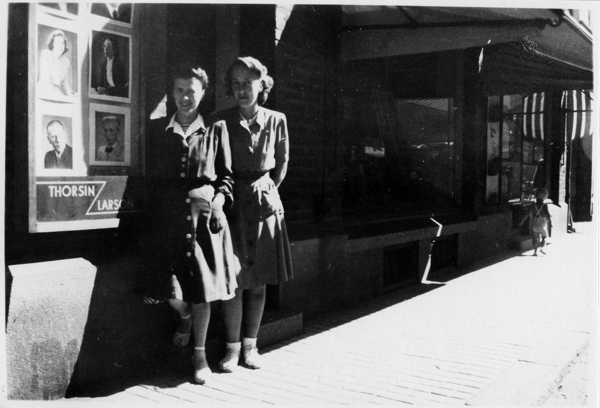 Två unga kvinnor i klänning som står utanför Thorsin-Larsons fotoateljé.