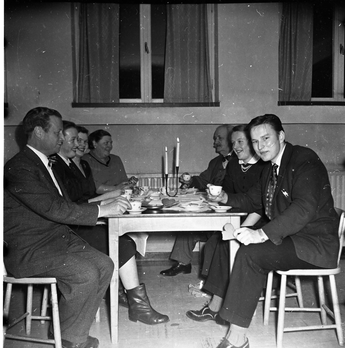 Män och kvinnor sitter vid kaffebord med tända ljus. Närmast till vänster Allan Berggren och som trea Eivor Åberg, därnäst Vivan Johansson. Till höger längst ned till höger A E Bolling och därnäst Ulla Jonasson.
