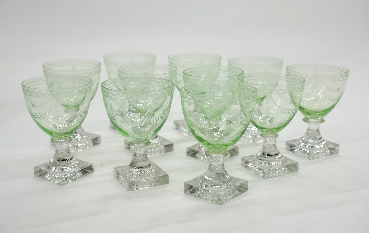 Starkvinsglas med cuppa av svagt grönfärgat glas och stumpad äggform, med graverad kantbård. Ben och fot av ofärgat glas. Ben med enkel bats, fyrkantig fot.