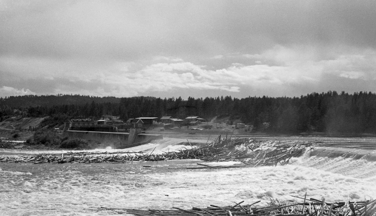 Tømmerfløting i Skjefstadfossen i Glomma sommeren 1947. Bildet er tatt fra østsida av elva mot terskeldammen som løftet vannspeilet i det ovenforliggende elvepartiet og bidro til å skaffe vann til kraftverket i bakgrunnen. Bildet viser også hvordan fløtingstømmeret bandt seg i hauger på steinører like nedenfor dammen, både midt i elveleiet og langs det østre landet (i forgrunnen).