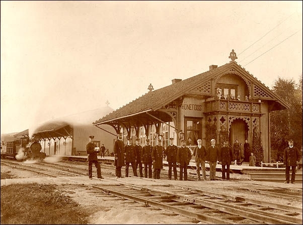 Jernbanepersonalet foran Hønefoss stasjon. I bakgrunnen damplokomotiv type XV med blandet tog
