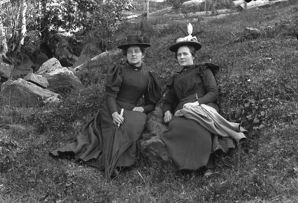 To unge damer med hatt sitter på bakken.