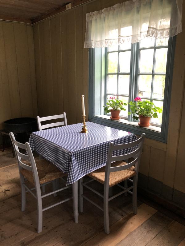 Kafebord inne på Lømo med blårutete duk og geranium i vinduet.