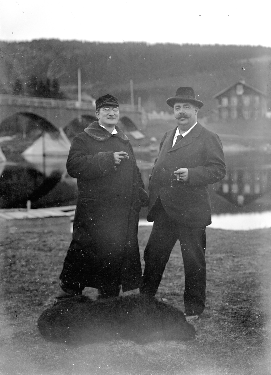 To menn og en hund foran bru over elva.  Til venstre: Doktor (distriktslege i Trysil) Otto Mejlænder (1865-1944).