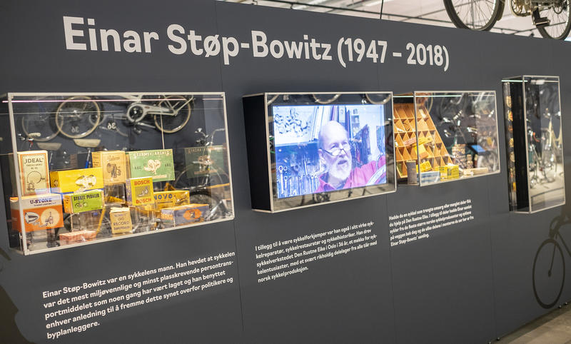 Utsnitt av utstilling om sykler og Einar Støp-Bowitz på Norsk kjøretøyhistorisk museum. Vegg med tekst, montere med diverse gjennstander og en skjerm med bilde av Einar Støp-Bowitz.