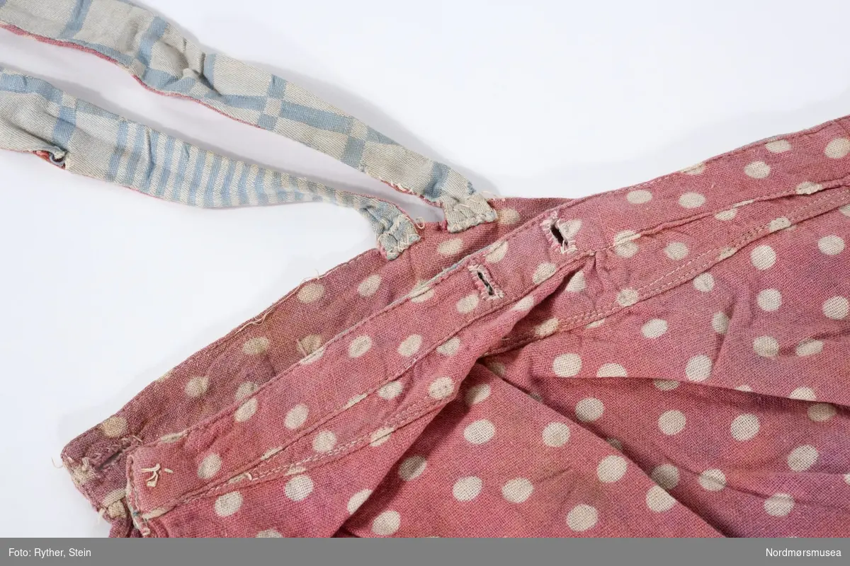 Rosa ballongbukse med hvite dotter og seler. Selene og linning mangler knapp. Selene og linning bak foret i blåmønstret stoff.