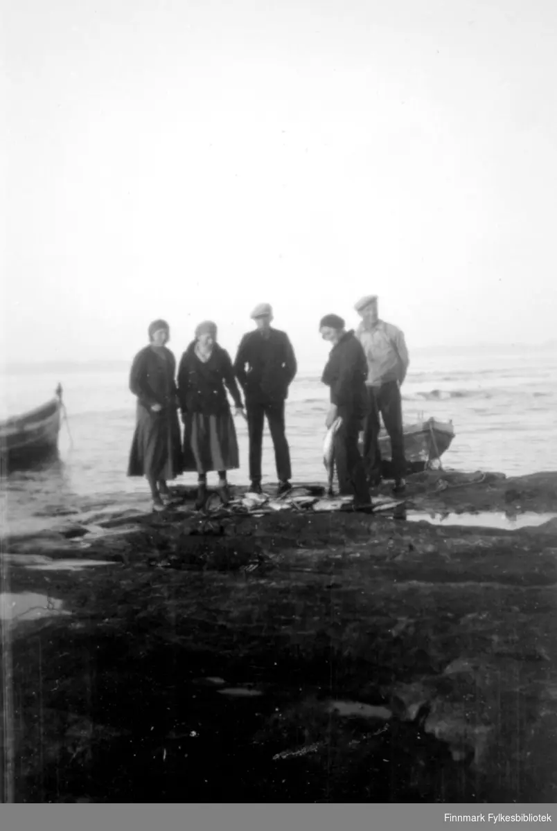 Tre damer og to menn ved fjæra i Salttjern, to båter i bakgrunn. 