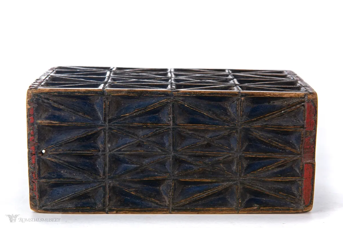 Et geometrisk mønster sammenkomponert av kryss skåret ut i dyp karveskurd på alle eskens sider. Nederst på esken er det skåret ut en tannbord.