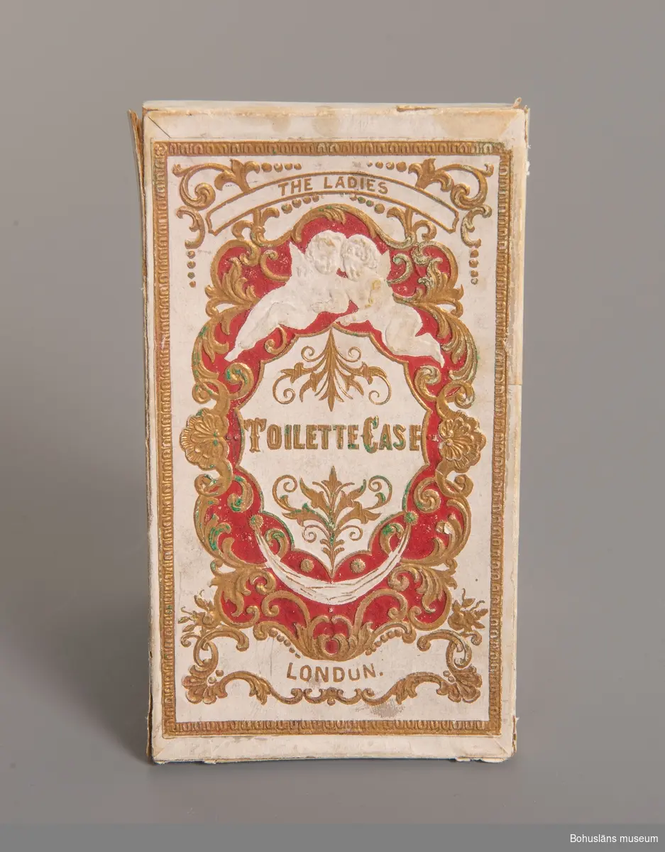 Ask med texten:"Toilette Case The Ladies  London".
På locket rik tryckt och pressad dekor i vitt, rött och guld.