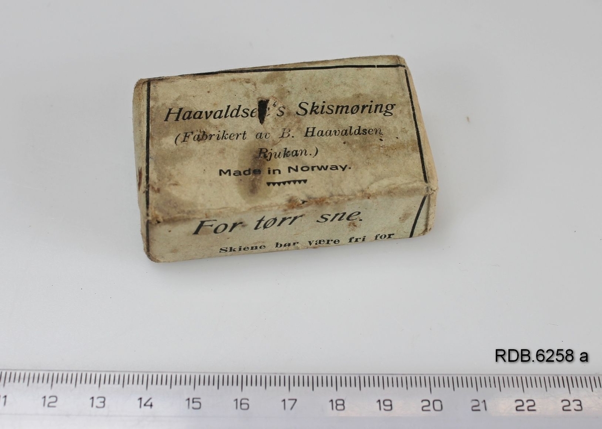En uåpnet, rektangulær pakke med Haavaldsens Skismøring. Innpakket i grått papir med svart påskrift.