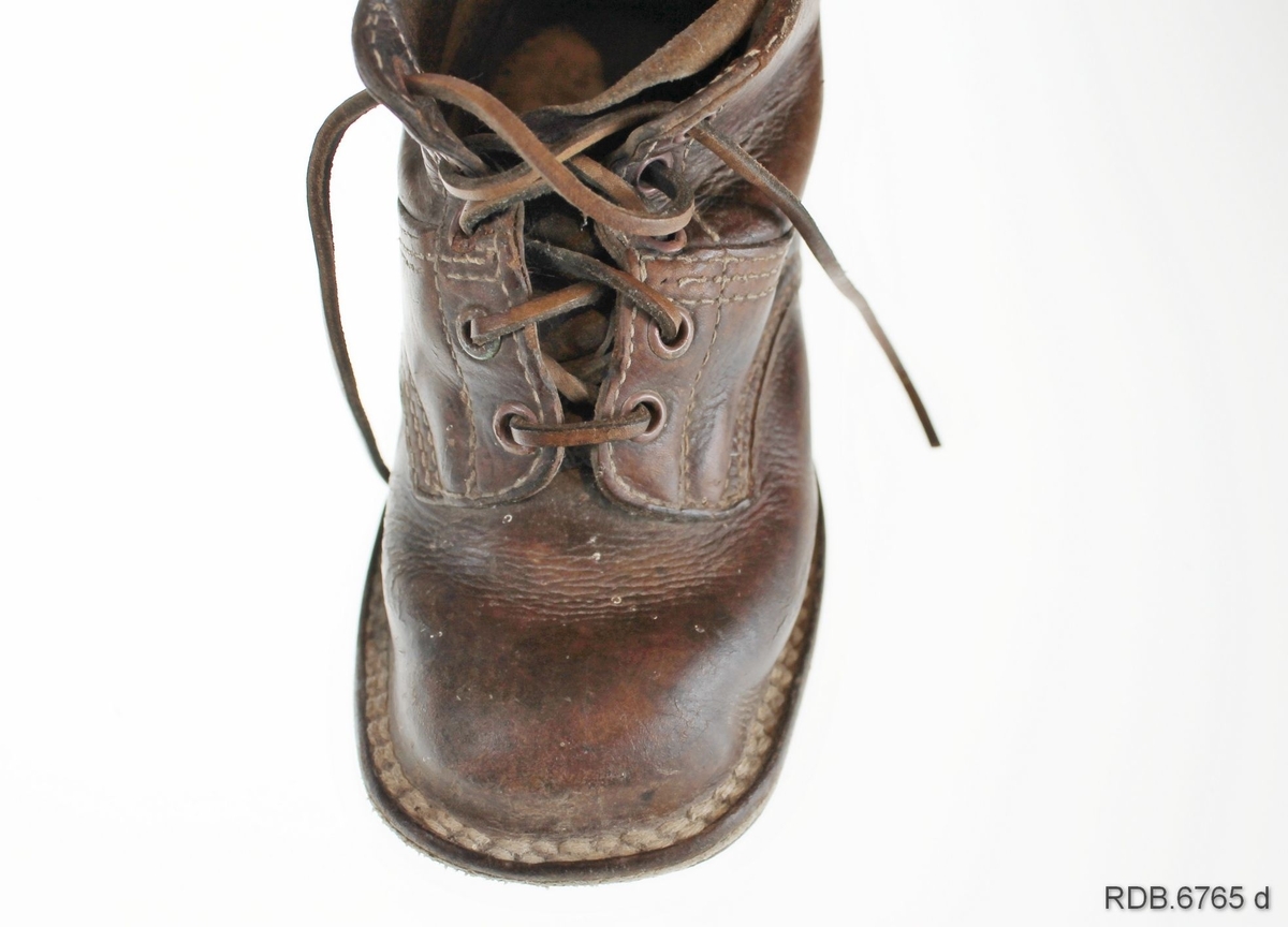 Et par brune barnesko laget av en bygdeskomaker. Skoene har åpning med tunge foran og lukkes med skolisser i lær tredd gjennom 5 par maljer. Skoene er randsydde. Det er slitt hull på sålen under venstre sko.