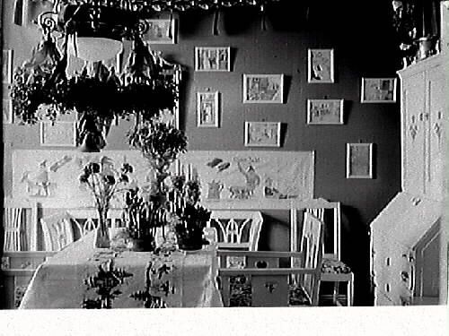 Interiör med bokhyllor och soffgrupp på ena bildedn. Bild 2 (GB2_2728) visar ett rum med mörka väggar fyllda av småtavlor och ljust målade trämöbler i stram jugendstil. Blombuketter hänger i taklampan och står i vaser på bordet, som täcks av en julduk. Ovanför den lilla soffan sitter en långsträckt bonad med julmotiv. Läroverksadjunkt Essén beställde bilderna, som troligen är tagna hos honom, se även bildnr GB2_2729.