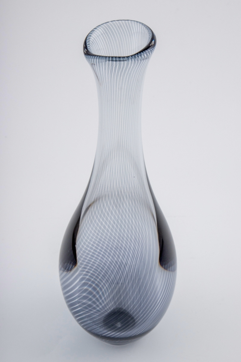 Høyreist dråpeformet vase i "Graalglas". Vasen er dekorert med spiralformede striper i underfangsteknikk, hvor det oppstår en optisk effekt i mønsteret ved å veksle mellom gråfargede og klare partier.