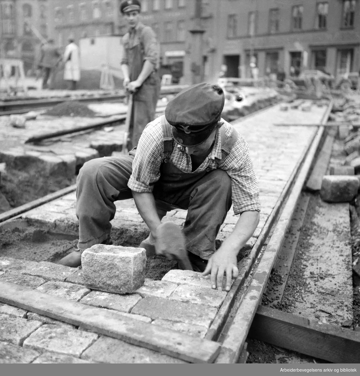Sporveisarbeidere. Legging av brostein/trikkeskinner på Jernbanetorget. Antatt 1950 - 1955.
