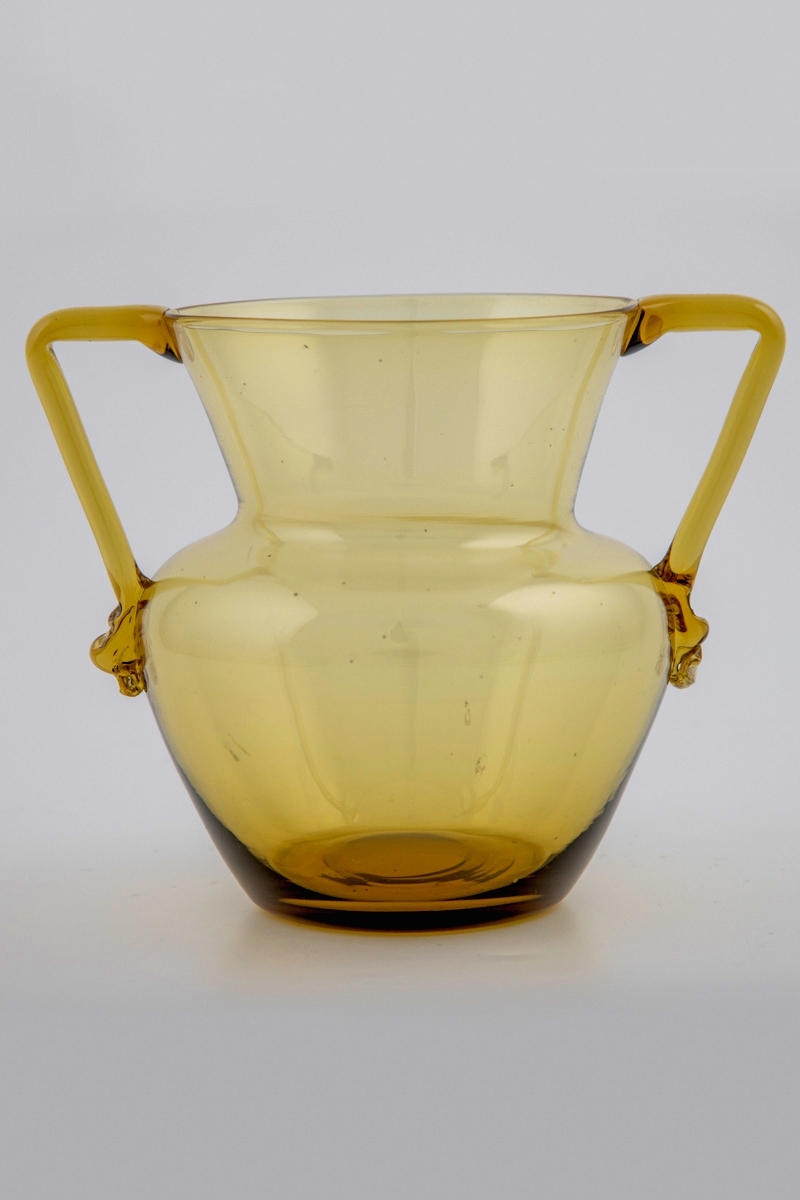 Amforaformet vase i gjennomskinnelig gulgrønt glass. Kuleformet korpus og konisk hals, to bøyde glasstaver fungerer som påsatte håndtak. Puntemerket delvis bortslipt