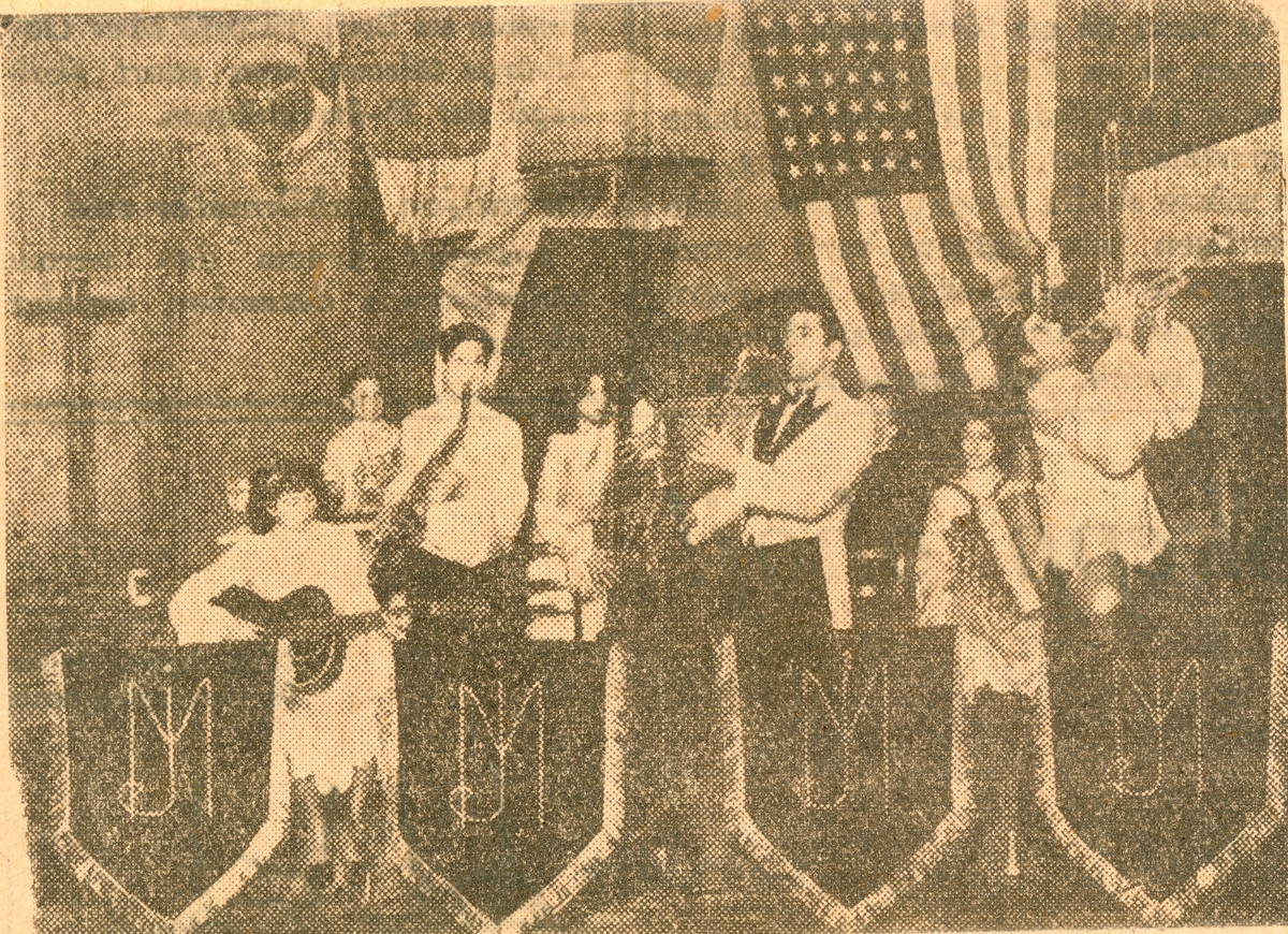 En orkester med olika instrument står på en scen och spelar musik. Bilden kommer från en urklippt tidningsannons för Jack Millons orkester.