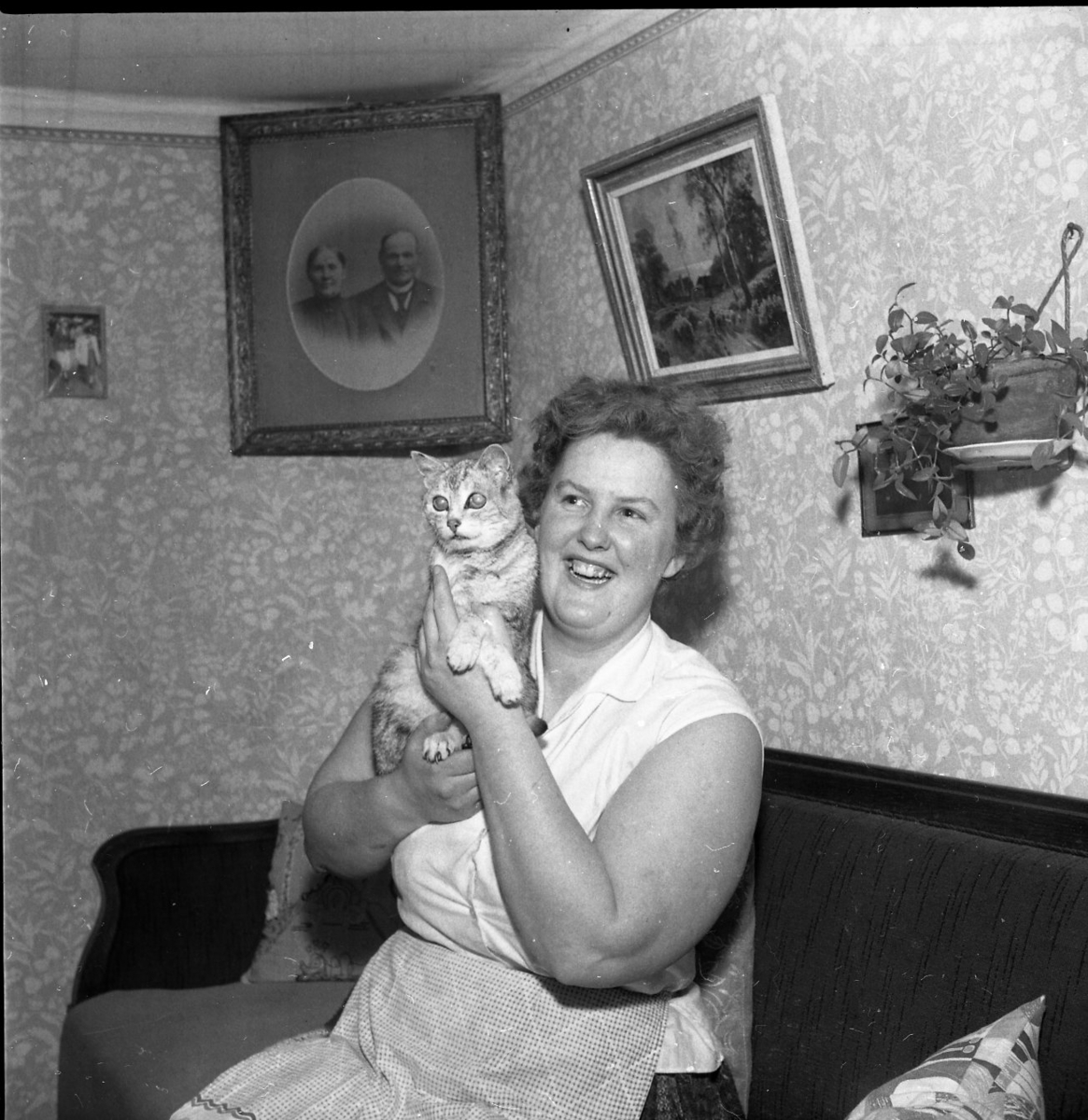 Laila Nyqvist sitter i soffan i sitt hem med katten Tutti i famnen.