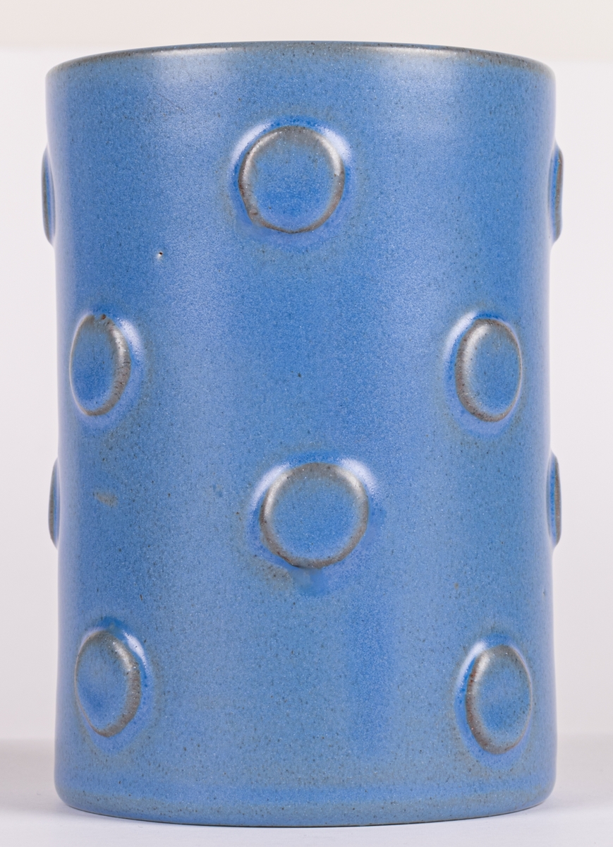 Vas, Bo Fajans, formgivare Eva Jancke-Björk. Cylindrisk med ettöringstora, runda, reliefplattor på ytan. Blå glasyr.