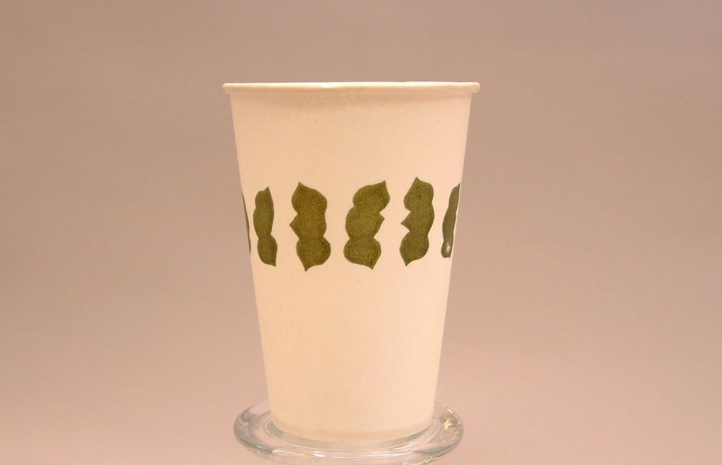 Vit pappersmugg med olivgrönt mönster på mitten som påminner om löv.
Mönstret kan vara ett feltryck av mönstret i Jvm18640-5.