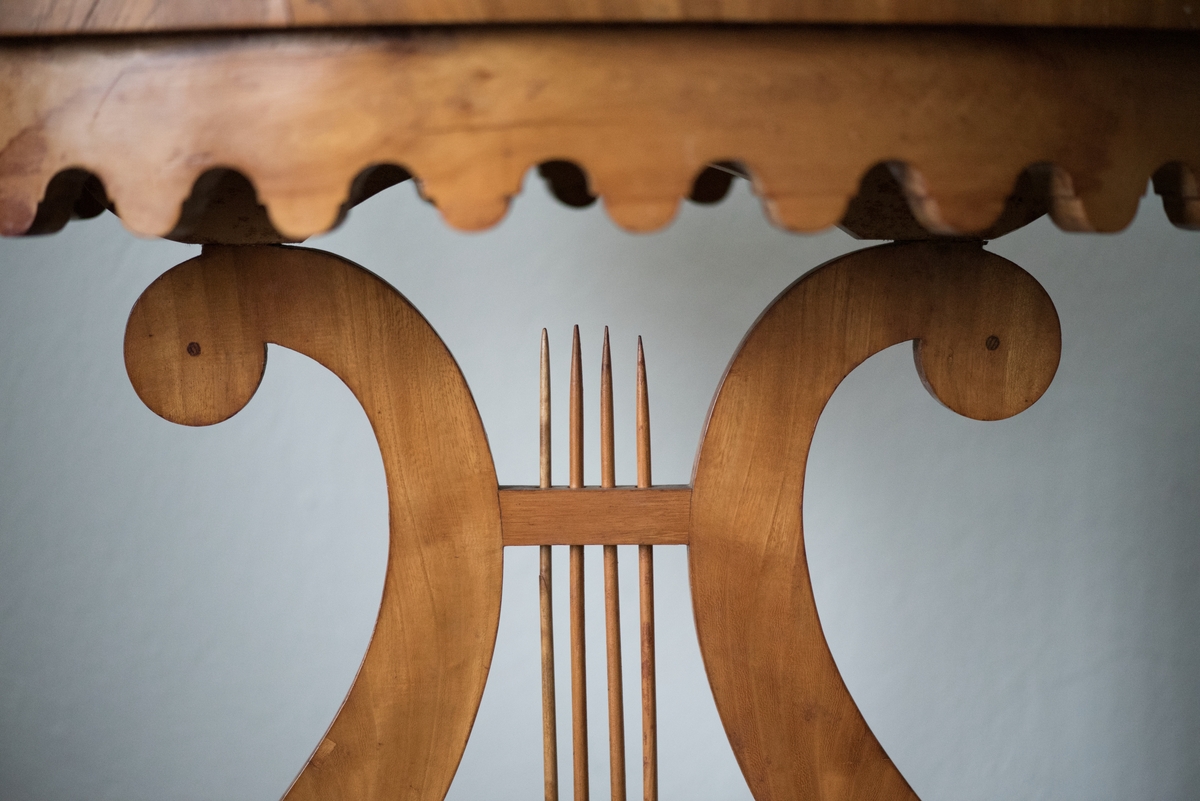 Bord av alm med oval bordskiva och ben i form av en lyra med strängar. Bordsskivan har inläggningar av intarisia, i form av en stjärna. Bordsskivans sarg är vågformad. Fotplattan är rektangulär och står på fyra korta, svarvade fötter.