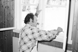 Mann som maler vinduer i en Frøystul-hytte.