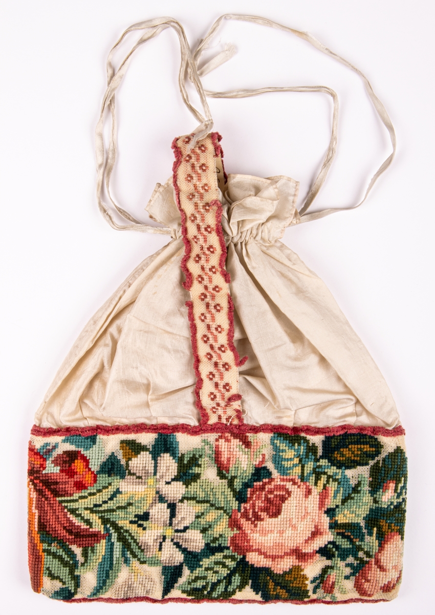 Väska i siden med broderad bård på stramalj, rosor i olika färger. 
Påsmodell, band att dra ihop och bära med.