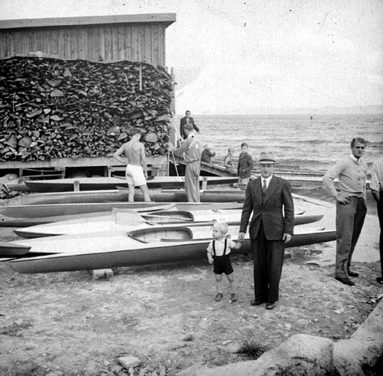Vid ett skjul med en vedstapel intill ligger några kanoter uppdragna på Vätterstranden som tillhör Jönköpings kanotklubb.