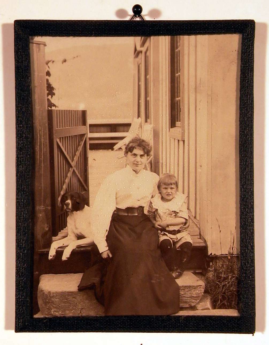 Fotografi av mor med sønn og hund på verandatrinnet en sommerdag.