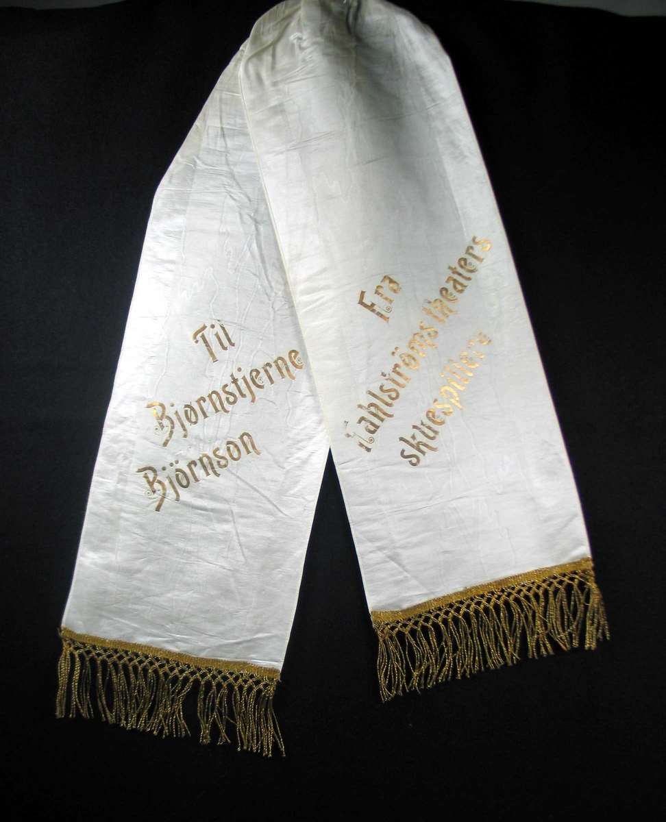 Begravelsessløyfe i hvit silke med frynser og tekst i gull.
