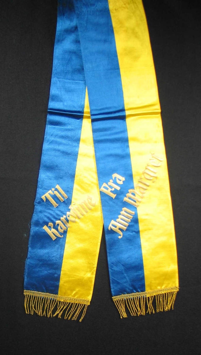 Begravelsessløyfe i gul og blå silke med tekst og frynser i gull.