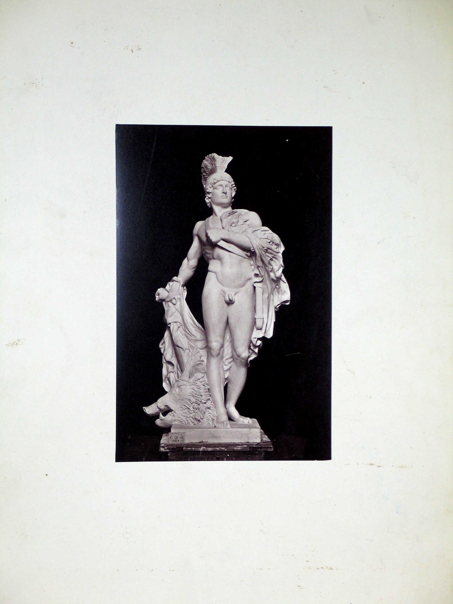 Fotografi av en skulptur limt på kartong.  Spikermerker øverst og nederst.