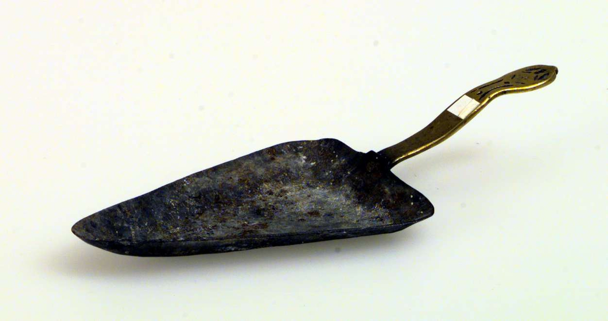 Askebeger formet som en liten peisspade. Håndtaket er av messing, spaden av jern.