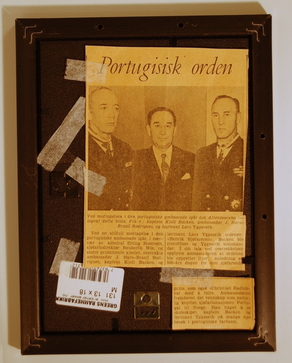 Fotografi i sort plastramme  med glass. Avisklipp festet på baksiden.