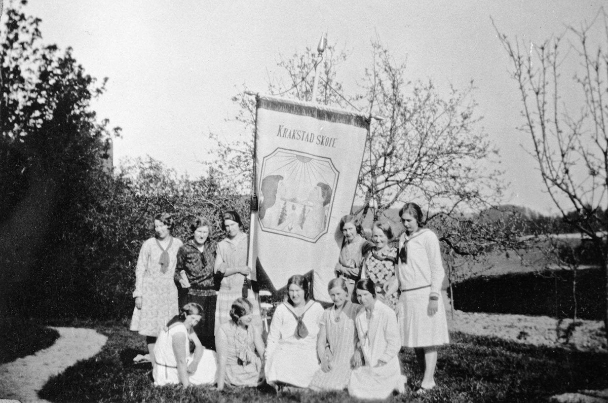 Overlevering av skolefanen til Kråkstad skole 17. mai 1930. 11 kvinner/jenter samlet rundt fanen.
