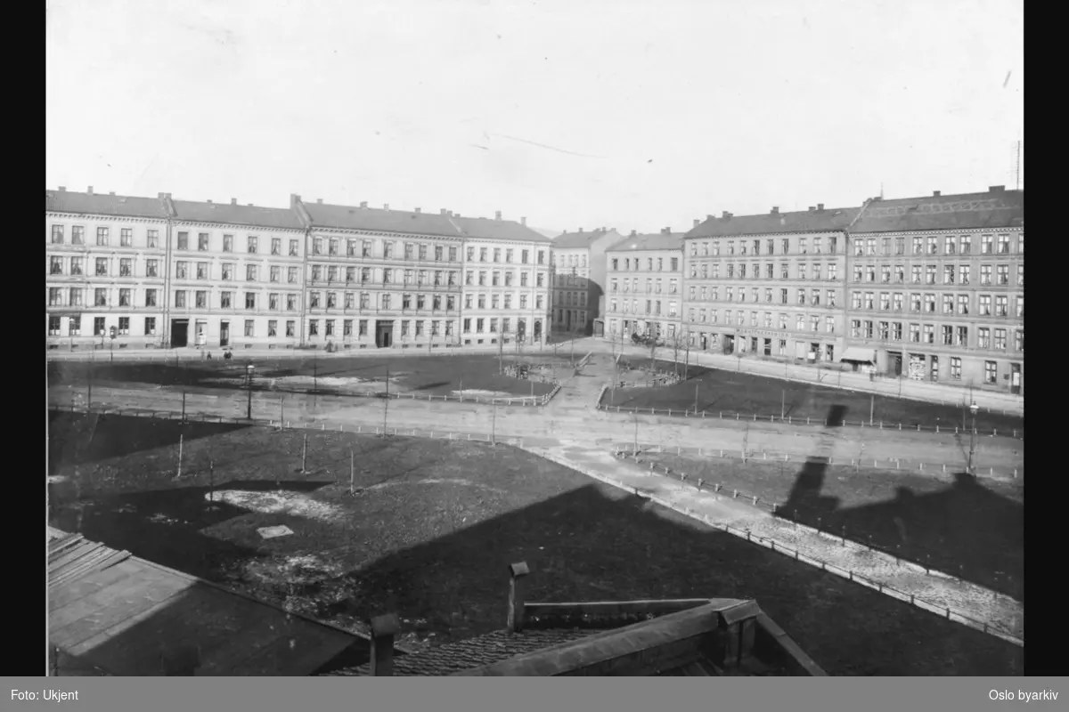Parkområde på Schous plass med gangveier og plener. (Parklagt 1915 - 1916). Bygårder i Nordre gate (til venstre) og Toftes gate. Diverse butikker.