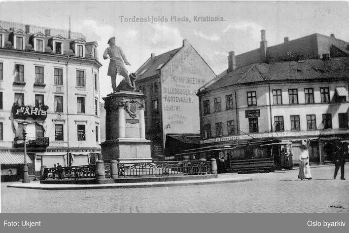 Tordenskiolds plass med statuen av Peter Wessel Tordenskiold (fra 1901, av Axel Ender). Trikk. Hotel Paris, reklamevegg, butikker, butikkskilt. Postkort.