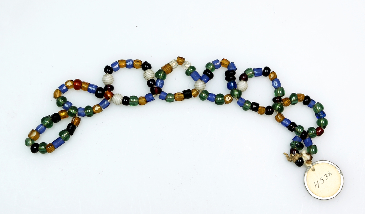 Perler i ulike farger og utforming tredd på snorer, som er tvunnet og knytt i mønster